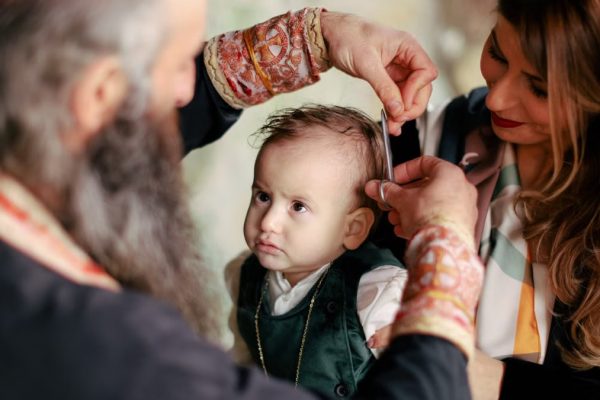 A baby's first haircut performed during a religious ritual with parents and clergy present.
