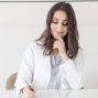 A female nutritionist in a lab coat writing notes with an apple and plant on the desk.
